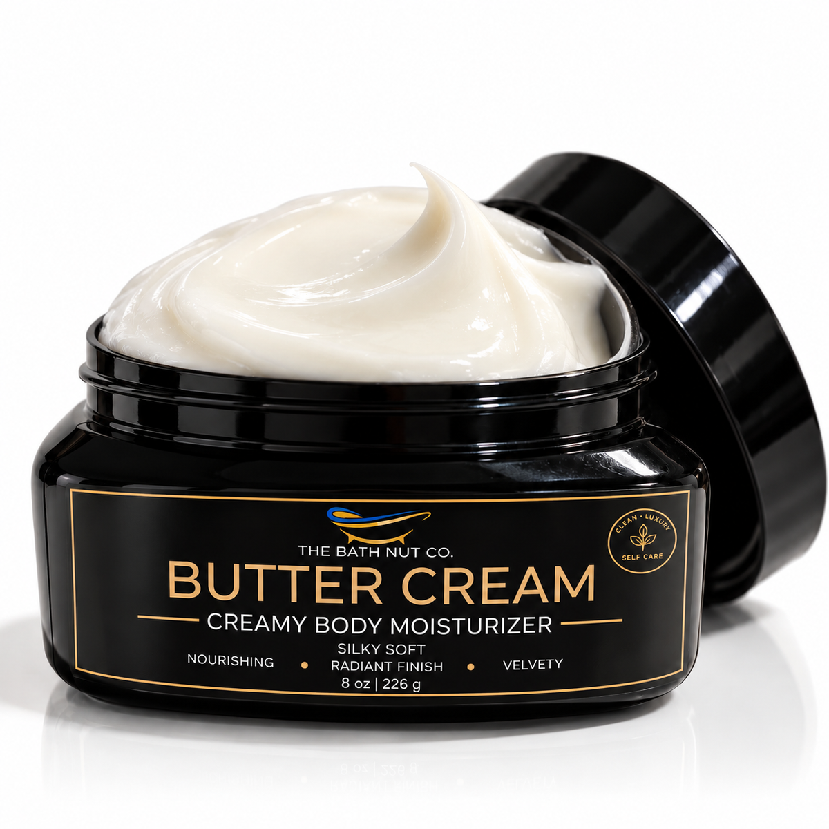 A jar of Butter Cream by The Bath Nut Co. on a white background, showing the creamy off-white body moisturizer inside a glossy black jar with its lid leaning behind it. Main image